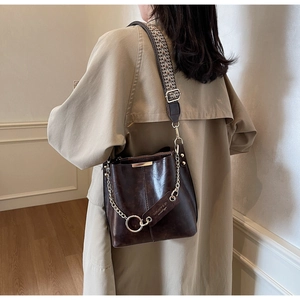 Détail du sac seau marron foncé avec bandoulière tissée et chaîne dorée