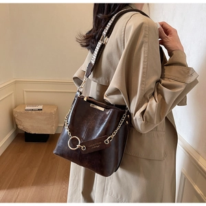 Détail du sac seau en cuir marron foncé avec bandoulière pied-de-poule et chaîne