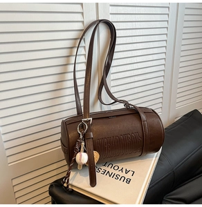 Detail of dark brown cylinder bag with letter embossing and baseball charm accessory