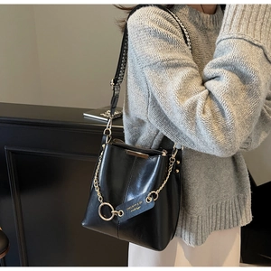 Détail du sac seau en cuir noir avec chaîne dorée et bandoulière géométrique