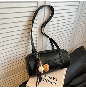 Detail of black cylindrical underarm bag with embossed letters and a sports charm