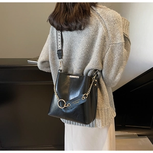 Détail du sac seau en cuir noir huilé avec bandoulière tissée géométrique et chaîne dorée