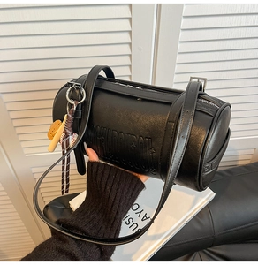 Detail of black cylindrical shoulder bag with embossed letters and baseball charm