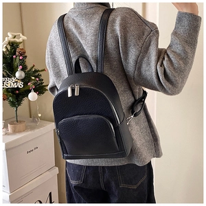 Detail of black pebbled leather texture and silver zippers on a mini travel backpack