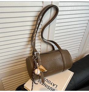 Detail of vintage brown cylinder bag with embossed letters and a baseball charm