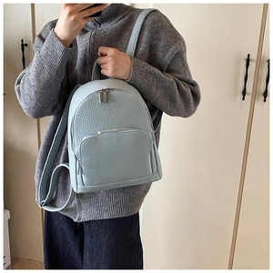Close-up of a light blue pebble leather backpack worn by a model in a minimalist room