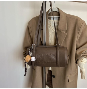 Detail of coffee brown leather cylinder bag with embossed letters and baseball charm