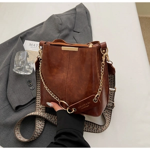 Détail d'un sac seau en cuir marron avec chaîne dorée et bandoulière géométrique
