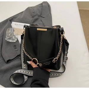 Détail du sac seau en cuir noir avec bandoulière géométrique et chaîne dorée