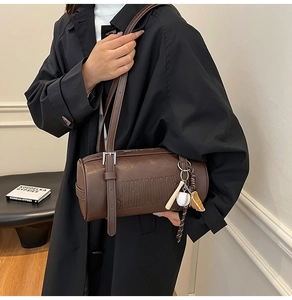 Detail of brown cylindrical shoulder bag with letter embossing and baseball charms