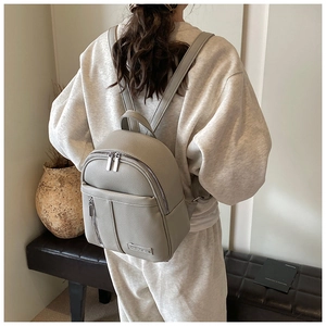 Detailed view of light gray pebble leather backpack with dual zippers and metal plaque