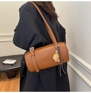 Detail of a brown cylindrical shoulder bag with embossed logo and a cute animal charm