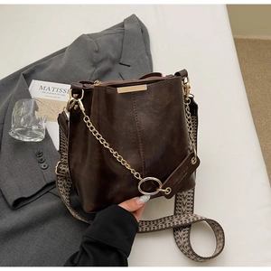 Détail du sac seau en cuir marron foncé avec chaîne dorée et bandoulière jacquard
