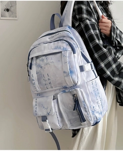 Detailed view of white backpack with blue ink floral pattern and multi-pocket design on model
