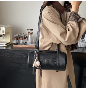 Detail of black cylindrical underarm bag featuring embossed letters and baseball charms