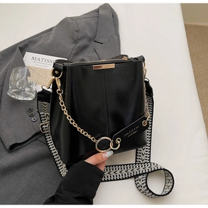Détail du sac seau en cuir noir avec chaîne dorée et bandoulière géométrique
