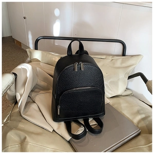 Close-up of black lychee grain leather mini backpack with silver zippers on a chair