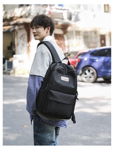 Outdoor shot of a black minimalist laptop backpack with adjustable side straps and logo detail