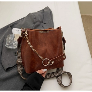 Détail du sac seau en cuir marron avec chaîne dorée et bandoulière tissée ethnique