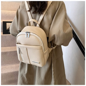 Detail of a creamy white pebbled leather backpack with metallic zip and brand plate