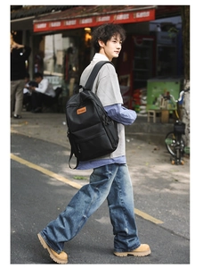 Close-up of black nylon travel backpack with orange logo and wide padded shoulder straps