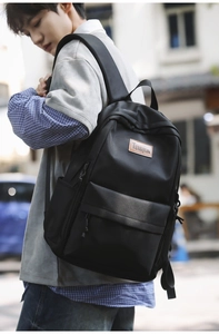 Detailed view of black minimalist backpack with brown leather brand tag on urban street