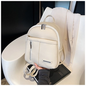 Close-up of beige lychee leather backpack with silver zippers on a white chair