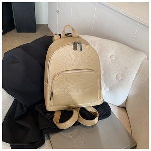 Close-up of beige lychee texture leather backpack with silver zippers on a soft sofa