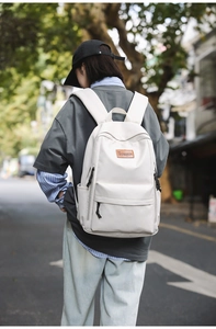 Outdoor view of a cream minimalist laptop backpack with a leather brand logo label