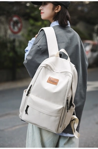Close-up of minimalist off-white backpack featuring brown leather logo and side pockets