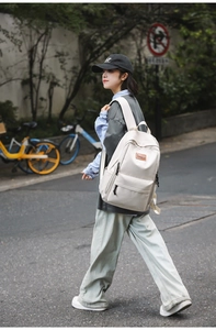 Outdoor shot of a beige canvas backpack with brown leather logo on a city street