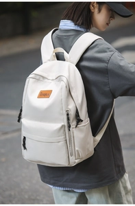 Outdoor close-up of a minimalist cream white backpack with leather logo and side pocket