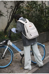 Outdoor shot of a beige minimalist backpack featuring a brown leather brand tag detail