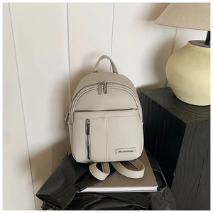 Detail shot of beige pebble leather mini backpack on books with metal logo plaque