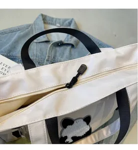 Dettaglio della cerniera nera e ricamo a forma di panda su una borsa tote in tela bianca