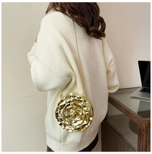 Detail of a gold metallic rose-shaped crossbody bag with a chain strap on a white sweater