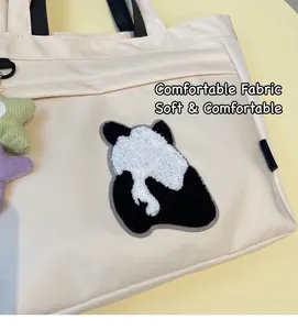 Dettaglio del ricamo a panda in spugna su borsa tote in tela crema con ciondoli a stella
