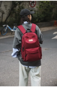 Detailed outdoor view of a deep red minimalist backpack with leather brand logo patch
