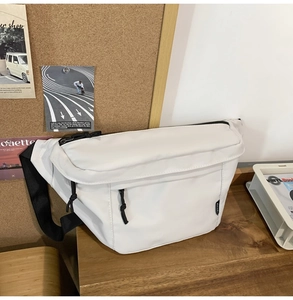 Detail of white nylon crossbody bag with black zippers on a minimalist wooden desk