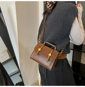Side view of dark brown crossbody bag with matte flap and gold metal buckles on a model