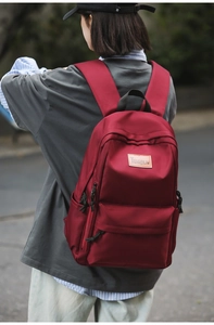 Detail view of burgundy nylon backpack with leather brand logo shown on person outdoors