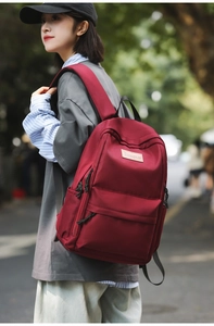 Detail of burgundy student backpack featuring adjustable straps and brand patch in street setting