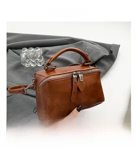 Detail of a brown leather handbag featuring dual zippers and a round padded handle