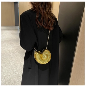 Chic shell-shaped gold acrylic evening clutch bag with metal chain strap on black coat