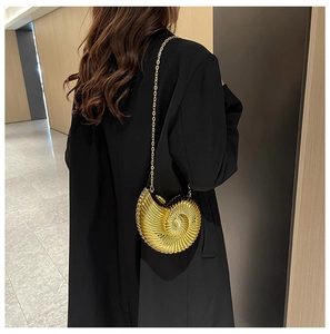 Detail of a golden snail-shaped acrylic clutch bag with a metallic chain on a black blazer