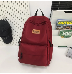 Detailed view of the burgundy nylon backpack with leather patch and zipper pockets