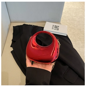 Detalle de bolso medialuna de acrílico rojo con asa circular y cadena dorada
