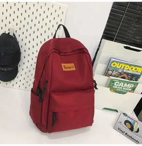 Detail of dark red canvas backpack with signature leather logo and black rope zipper pulls