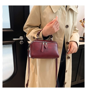Detail view of burgundy handbag featuring dual zippers and sturdy top handles on a trench coat