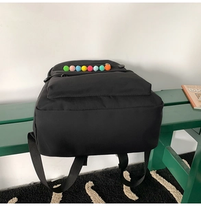 Detail of black backpack with colorful pom-poms on a green bench in a school setting